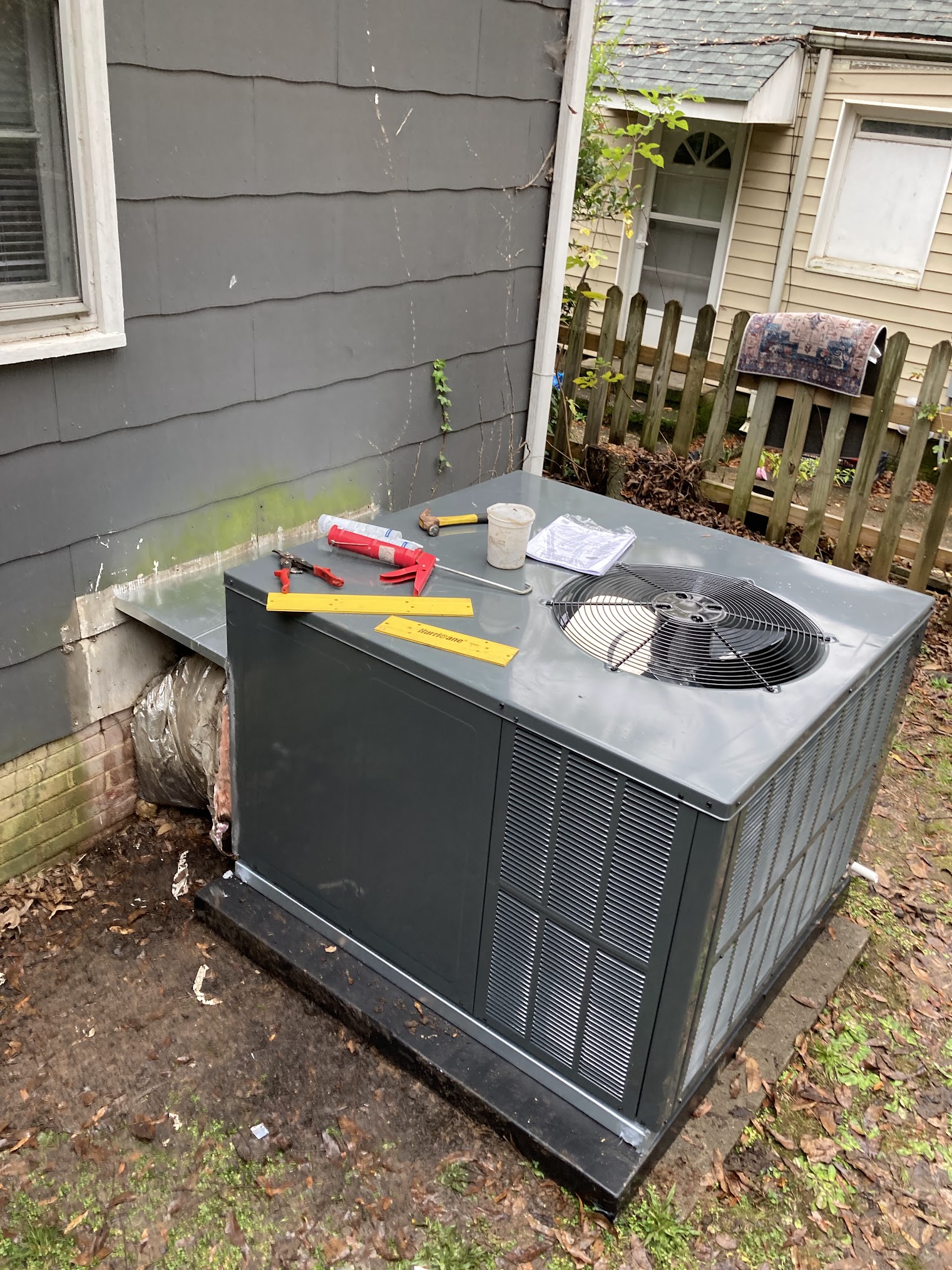 Gray package air conditioner beside a house, with tools still on top. Trade Servicez job photo.
